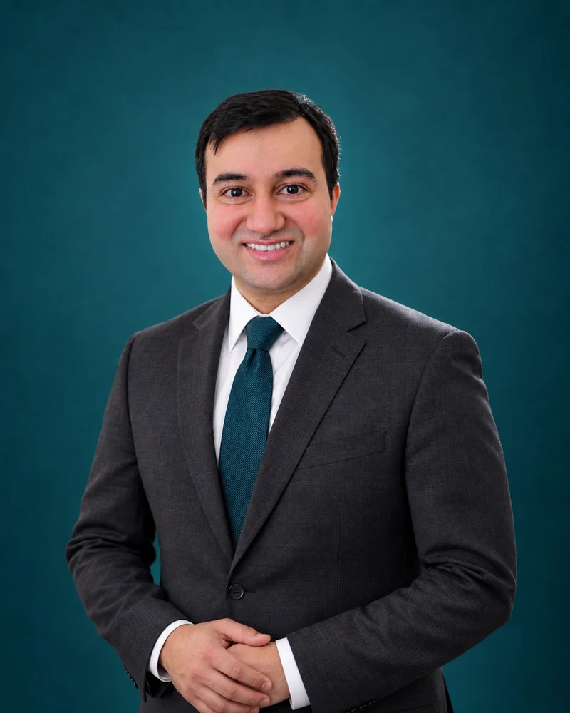 Professional portrait of Dr. Jameel Aftab in a suit against a teal background